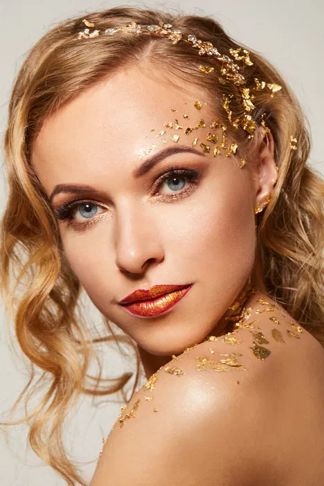 Blondynka z eleganckim makijażem i złotymi płatkami na twarzy i ramieniu, stylizacja glamour.