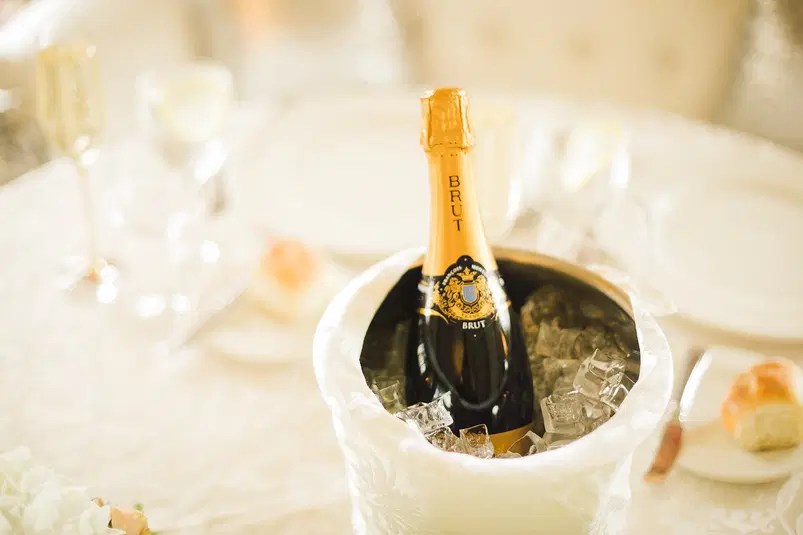  Butelka szampana Brut w wiaderku z lodem na elegancko nakrytym stole, kieliszki do szampana, wykwintna zastawa stołowa, luksusowa sceneria, przyjęcie. 