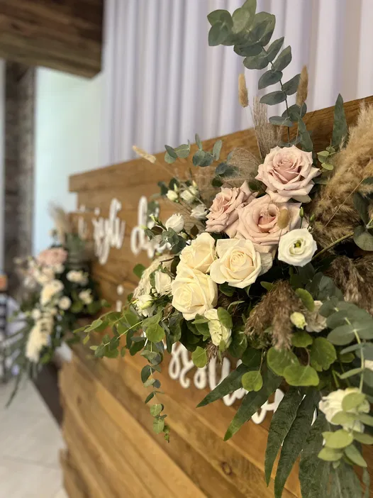 Dekoracja kwiatowa z białych i różowych róż na drewnianej ścianie z liśćmi eukaliptusa, eleganckie aranżacje weselne, rustykalny styl.