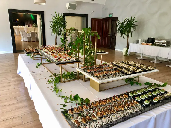  Luksusowa sala bankietowa z elegancko udekorowanym stołem cateringowym, pełnym różnorodnych przystawek, gotowa na wyjątkową imprezę lub przyjęcie weselne. 