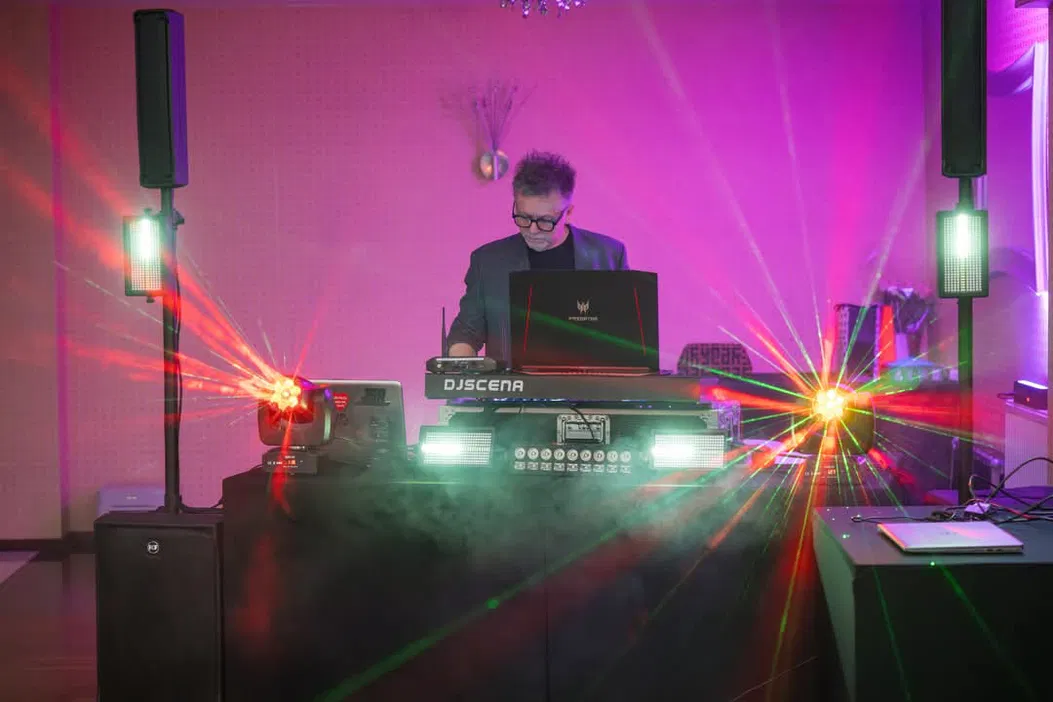 DJ grający muzykę na żywo, scena z efektami laserowymi i dymnymi podczas przyjęcia lub imprezy.