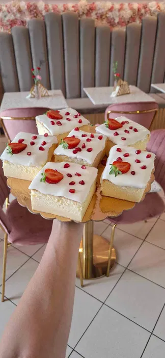 Ciasto z kremem i świeżymi truskawkami oraz granatem na złotej paterze, w eleganckiej kawiarni z różowymi akcentami.