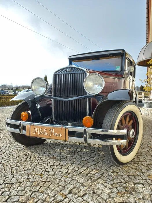 Retro samochód ślubny na brukowanej ulicy z tablicą Młoda Para.
