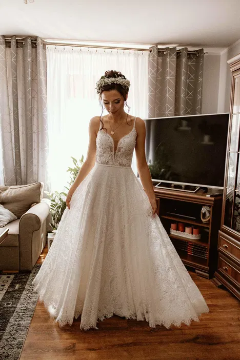 Panna młoda w białej koronkowej sukni ślubnej i wianku na głowie w eleganckim wnętrzu.