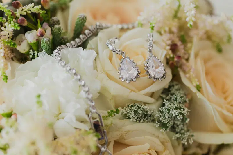  Eleganckie kolczyki z diamentami w kształcie łzy na tle bukietu ślubnego z białych róż i zielonych akcentów. 