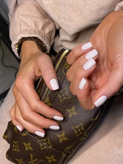  Dłonie z białymi paznokciami trzymające luksusową torebkę, elegancki manicure, modny dodatek, stylizacja. 