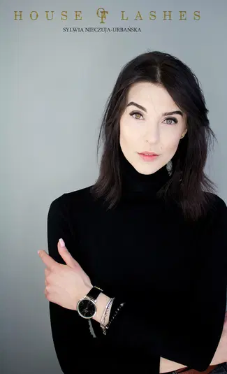  <span lang=pl>Kobieta w czarnym golfie z delikatnym makijażem i ciemnymi włosami, pozująca na szarym tle. Zegarek na ręku i logo House of Lashes w górnej części zdjęcia.</span> 