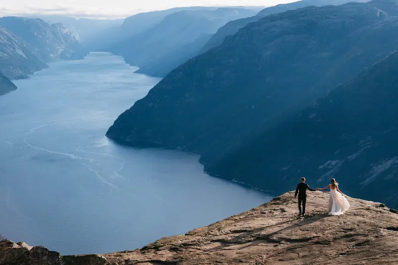  Para młoda na szczycie klifu z widokiem na panoramiczny fiord, sceneria górska, romantyczny ślub plenerowy. 