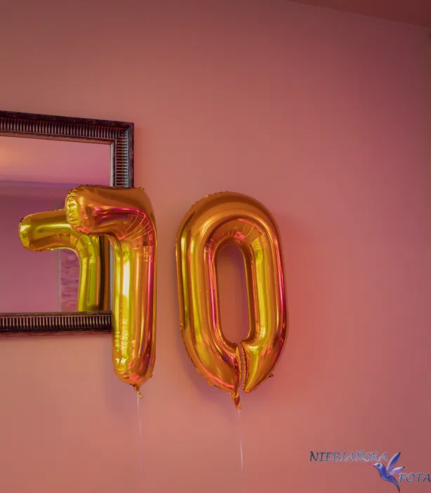 Balony foliowe w kształcie liczb 70 w kolorze złotym na tle lustra - dekoracja urodzinowa.