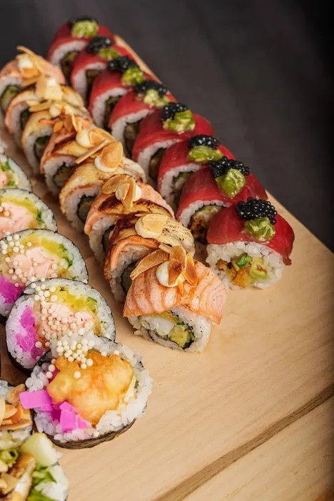 Różnorodne sushi na drewnianej desce, zawierające kawałki z tuńczykiem, łososiem i różnorodnymi dodatkami, takimi jak migdały i kawior, idealne dla miłośników kuchni japońskiej.