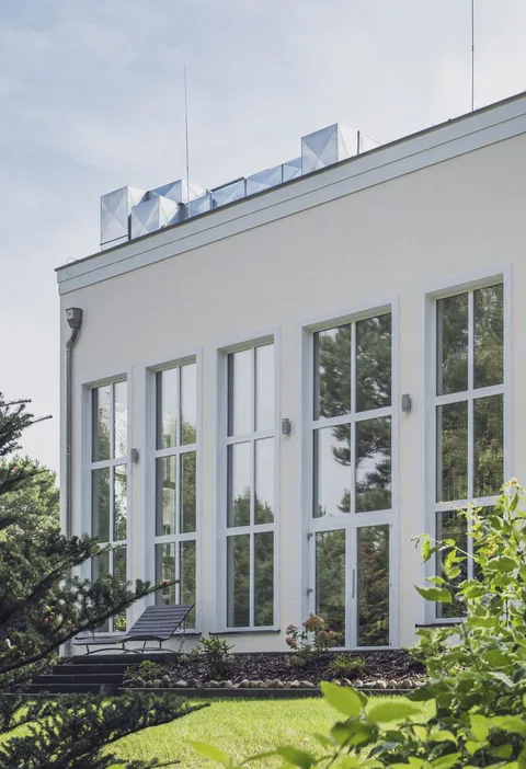 Nowoczesny biały budynek z dużymi oknami na tle zieleni, nowoczesna architektura, dom pasywny, energooszczędne okna.