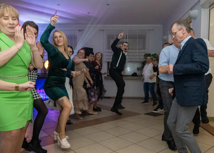  Grupa ludzi tańczących na przyjęciu w eleganckich strojach, radosna atmosfera na uroczystości w jasnej sali. 