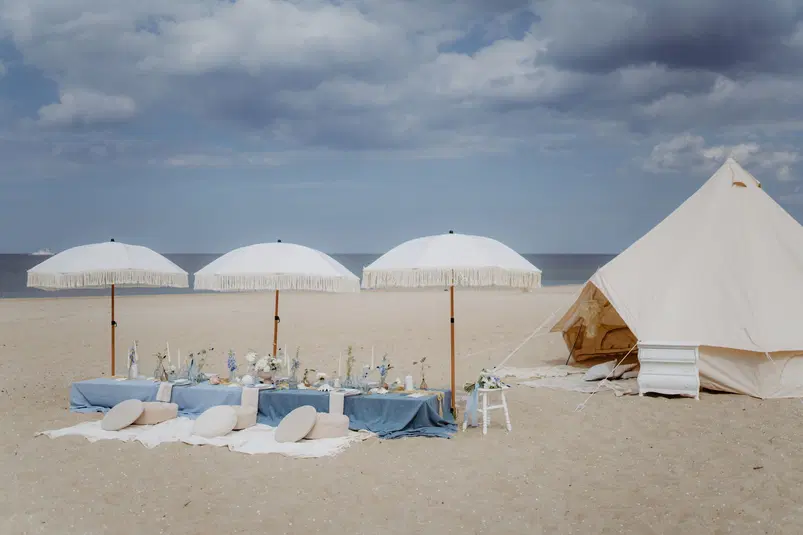  Romantyczny piknik na plaży z białymi parasolami i dekoracjami przy namiocie, idealne miejsce na relaks nad morzem. 