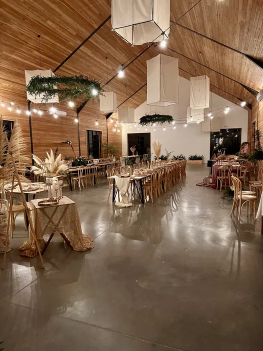 Elegancko udekorowana sala weselna z drewnianym sufitem i stylowym oświetleniem, ozdobiona zielenią oraz subtelnymi dekoracjami w naturalnych kolorach.
