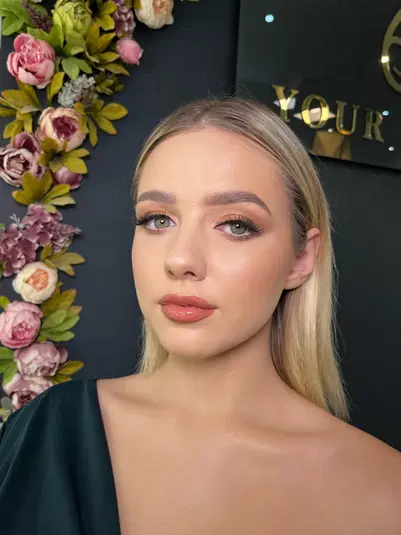  Blondynka w eleganckim makijażu na tle kwiatowej dekoracji. 