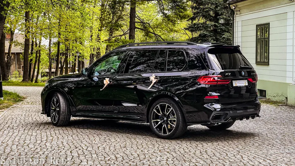  Czarny SUV BMW X7 ozdobiony na wesele, zaparkowany na brukowanej alejce w otoczeniu drzew, elegancki samochód ślubny na zewnątrz. 