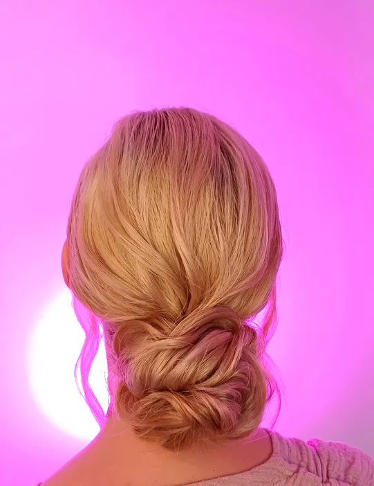 Blond włosy upięte w elegancki kok na tle różowego światła, stylizacja fryzura wieczorowa.