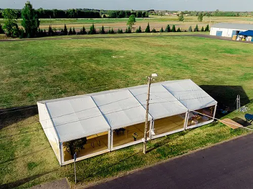  Duży biały namiot eventowy na zielonym polu, widok z lotu ptaka, wynajem namiotów, organizacja eventów na świeżym powietrzu. 