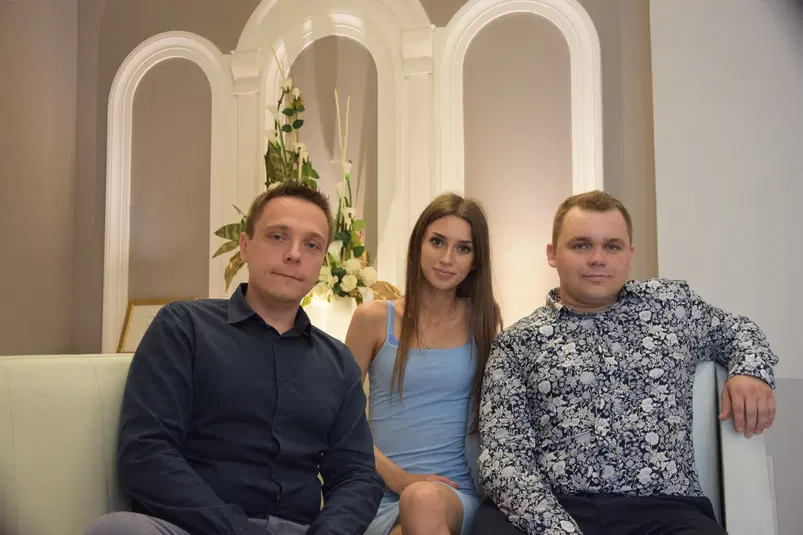  Trzy osoby siedzące na kanapie w eleganckim wnętrzu z kwiatową dekoracją w tle. 