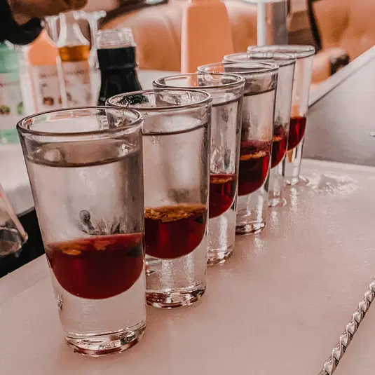  Sześć kieliszków z czerwonym alkoholem ustawionych w rzędzie na blacie barowym. 