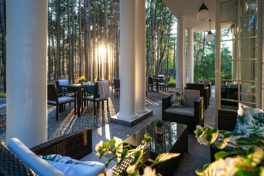 Taras w leśnym otoczeniu podczas zachodu słońca, ustawione meble ogrodowe, eleganckie poduszki, spokojna atmosfera na świeżym powietrzu.