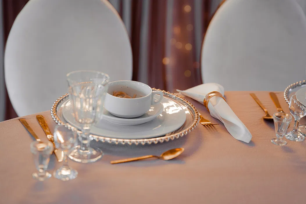 Elegancko udekorowany stół restauracyjny z porcelanową zastawą, kryształowymi kieliszkami i złotymi sztućcami na tle romantycznego oświetlenia.