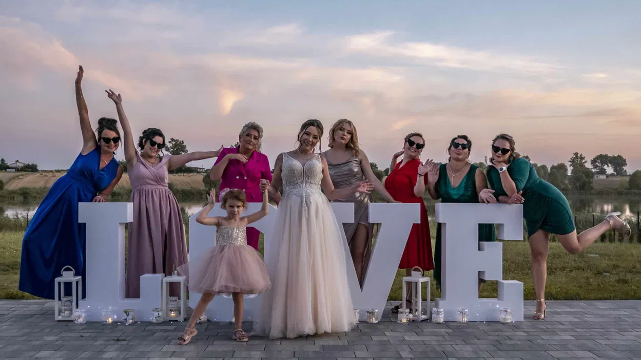 Panna młoda z druhnami i dziewczynką na świeżym powietrzu przy dekoracji LOVE podczas zachodu słońca.