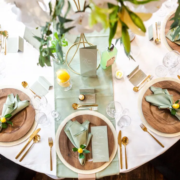 Stół udekorowany w motywie ślubnym z zielonymi serwetkami, złotymi sztućcami oraz menu, eleganckie przyjęcie weselne.
