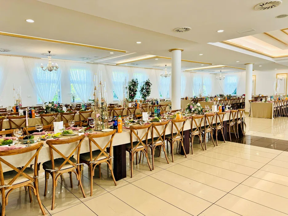 Przestronna sala weselna z elegancko udekorowanymi stołami, ozdobiona kwiatami i świecami, przygotowana na przyjęcie gości.
