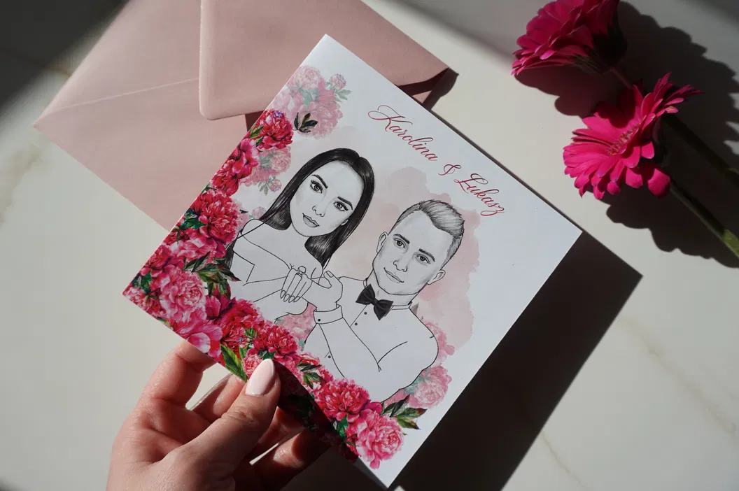 Ręcznie rysowana kartka ślubna z portretem pary, otoczona różowymi kwiatami i elegancką kopertą, idealna na zaproszenie weselne.