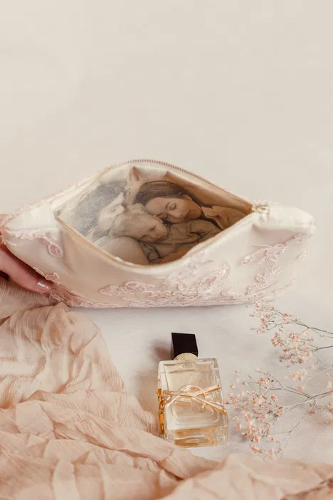 Różowa kosmetyczka z koronkowym wzorem, z otwartym wnętrzem ukazującym zdjęcie rodziny; obok flakon perfum oraz delikatne tkaniny i kwiaty - stylowe akcesoria codzienne.
