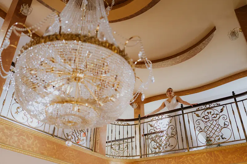  Luksusowy żyrandol w eleganckim wnętrzu z kobietą w sukni ślubnej stojącą na balkonie. 