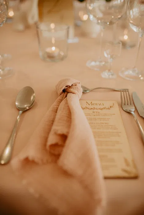Elegantne nakrycie stołu z menu, kieliszkami i różową serwetką na eleganckiej kolacji.
