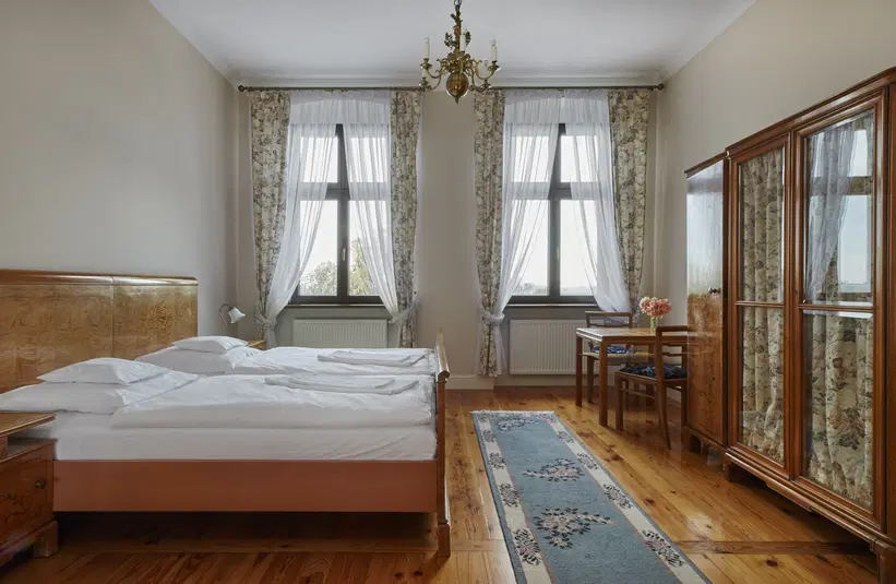  Stylowy pokój hotelowy z podwójnym łóżkiem, klasycznym wystrojem, drewnianą podłogą i dużymi oknami z firanami. 