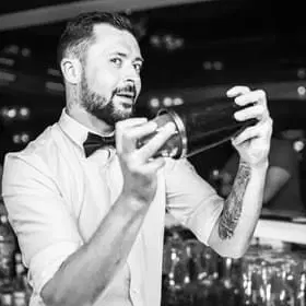  Barman w koszuli z muszką przygotowujący koktajl w barze, trzyma shaker do drinków, czarno-białe zdjęcie. 