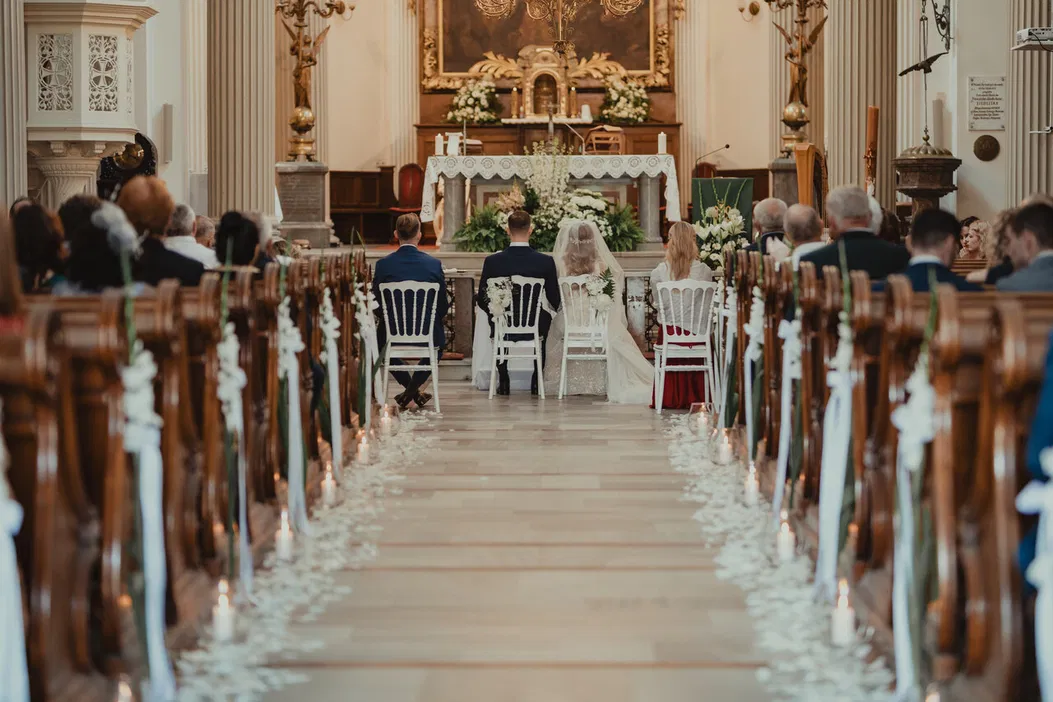 Ślub w kościele, para młoda przed ołtarzem, dekoracje kwiatowe, goście na ławkach, ceremonia zaślubin.