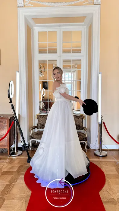 Kobieta w eleganckiej białej sukni na czerwonym dywanie w pomieszczeniu z lustrem.