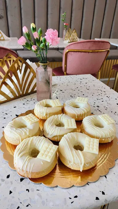 Pączki z białą czekoladą na złotej tacy w eleganckiej kawiarni z różami w tle.
