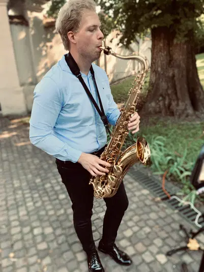  Muzyk grający na saksofonie na świeżym powietrzu w parku, ujęcie w lato, koncert na żywo, elegancki styl w niebieskiej koszuli. 