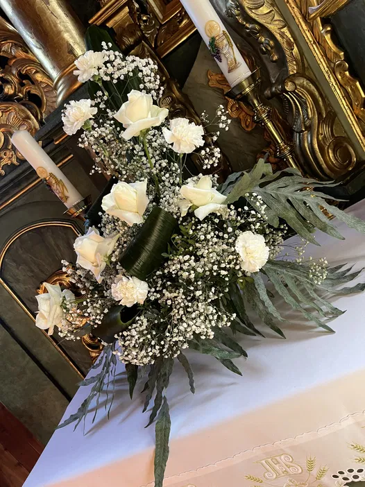 Bukiet białych róż i goździków z gipsówką na tle bogato zdobionego ołtarza w kościele.