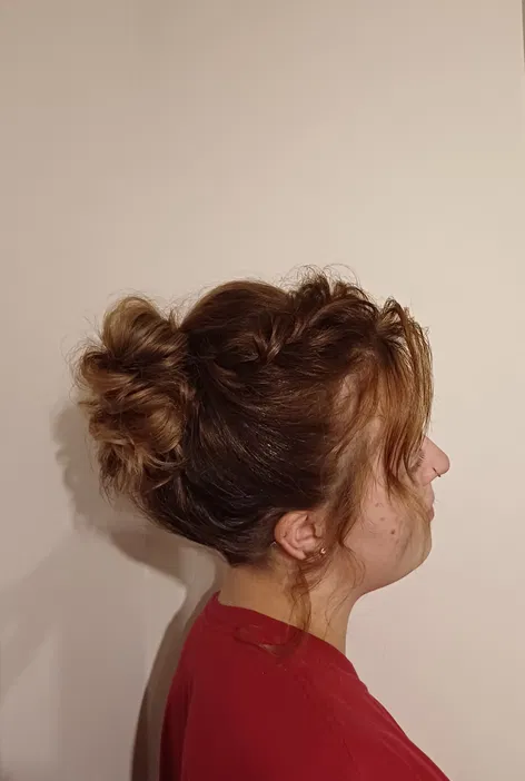 Kobieta z brązowymi włosami upiętymi w stylowy kok, profil boczny, jasne tło, czerwona bluzka.