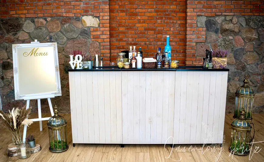  Rustykalny bar weselny ze ścianą z cegieł, dekoracje ślubne z butelkami alkoholu i napisem LOVE, elegancka tablica z menu, naturalne dodatki i lampiony. 