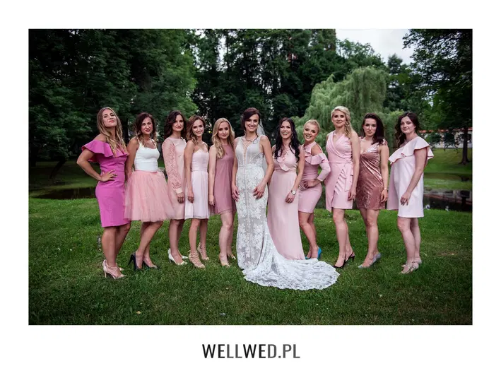 Grupa kobiet na weselu w eleganckich sukienkach, panny młodej w białej sukni ślubnej, na tle zieleni. 