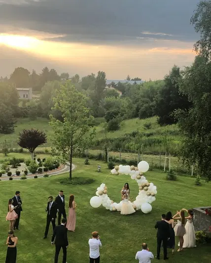  Uroczystość ślubna na świeżym powietrzu, zielony ogród, balony, ludzie w eleganckich strojach, zachód słońca. 
