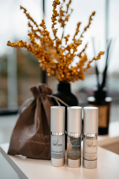 Produkty do pielęgnacji skóry na stole: serum, krem i żel oczyszczający Nature, w tle ozdobne suszone gałązki i lniany worek.