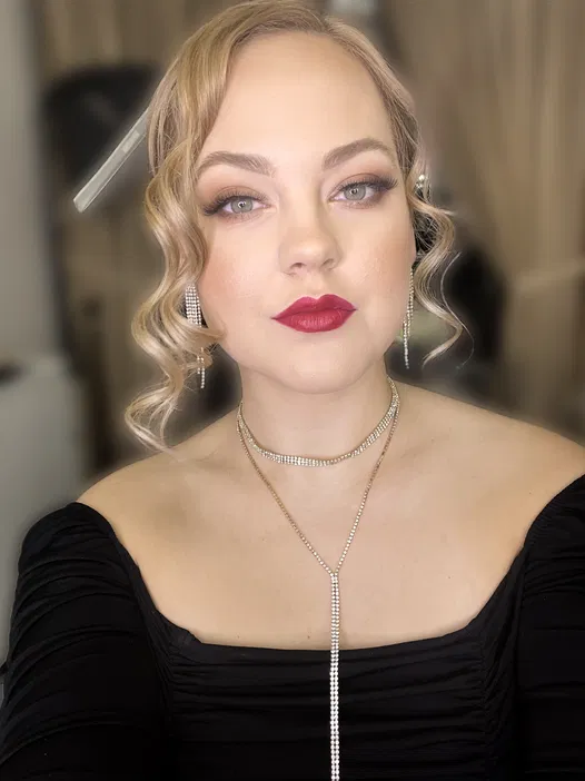 Blond kobieta z upiętymi włosami, makijażem glamour i czerwonymi ustami, w eleganckiej czarnej sukni, ozdobiona biżuterią, portret studyjny.