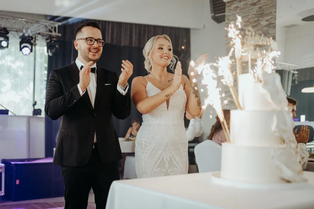 Para młoda celebrująca moment przy weselnym torcie z fajerwerkami, eleganckie wesele, para w strojach ślubnych.