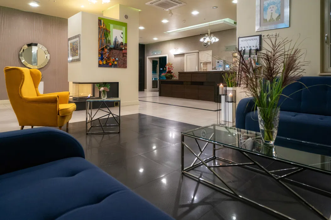 Stylowy hol hotelowy z żółtym fotelem, szklaną ławą i nowoczesnymi dekoracjami wnętrz.