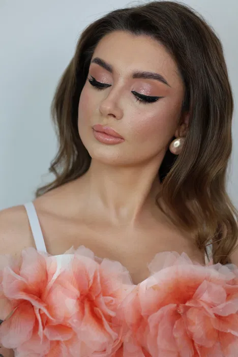 Piękna kobieta z makijażem w stylu glamour i sukienką ozdobioną różowymi kwiatami.