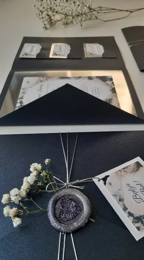  Eleganckie zaproszenia ślubne w granatowych kopertach z kwiatową dekoracją i wstążką, zdjęcie przedstawiające stylową papeterię ślubną. 